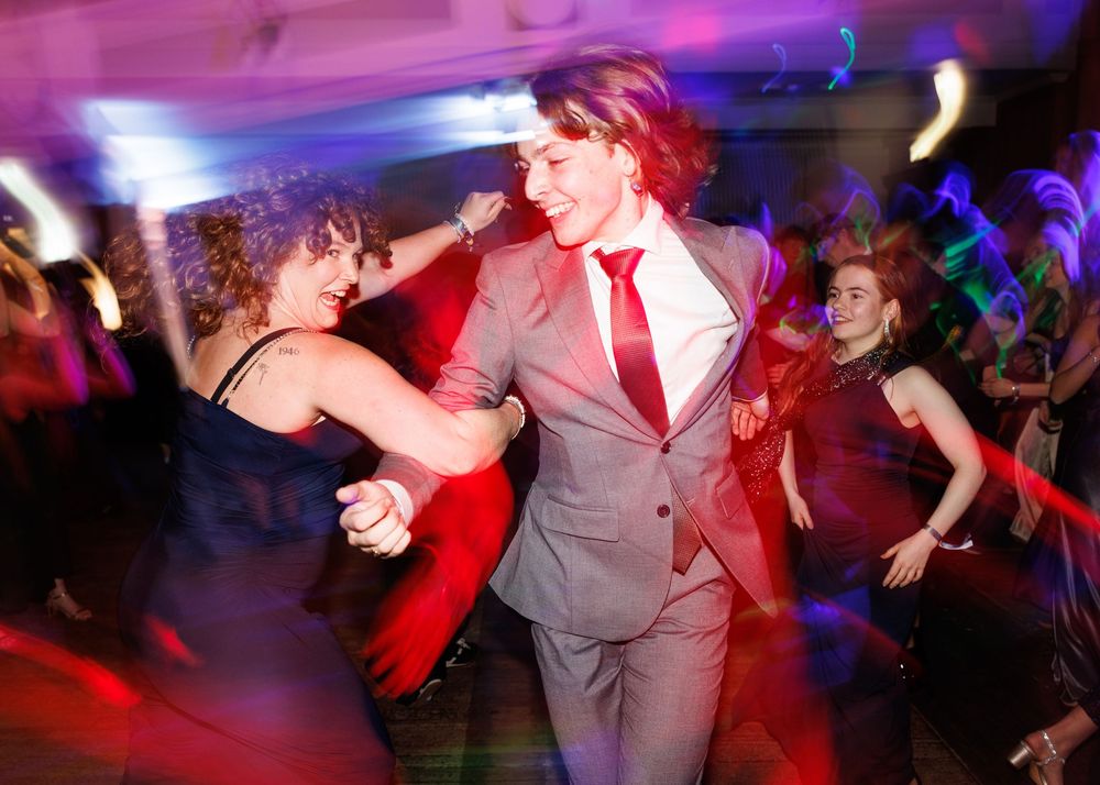 Dancers move energetically on a colorful dance floor illuminated by purple and red lights at a party venue.