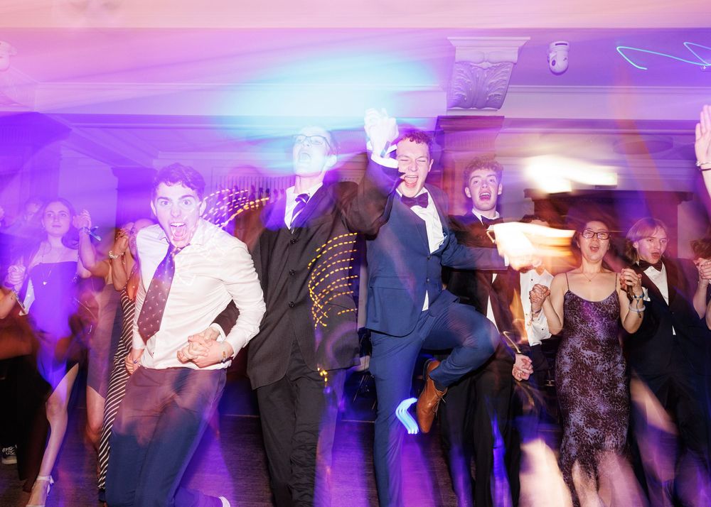 People dancing together at a party with purple and pink lighting creating a festive atmosphere.