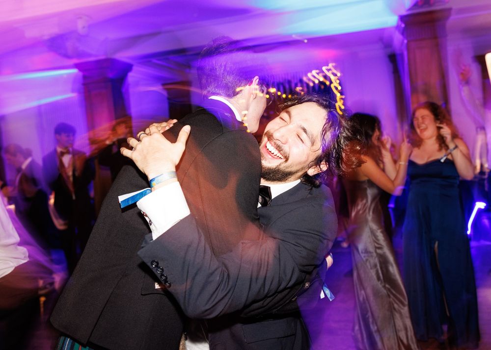 People dancing and celebrating at a wedding reception with purple and blue lighting effects.