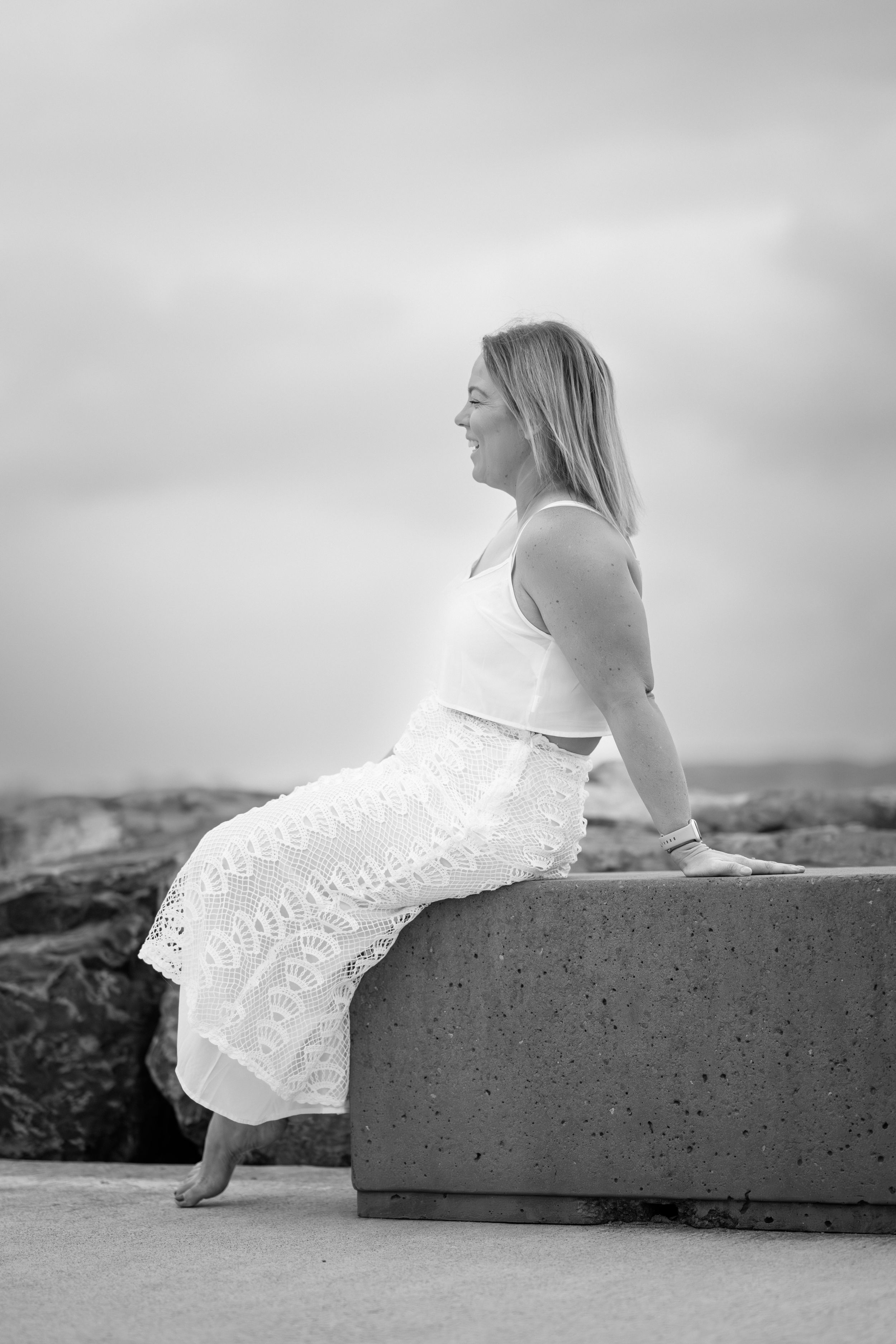 A series of black and white photos showing a person in a white dress reclining on a concrete surface near the ocean.