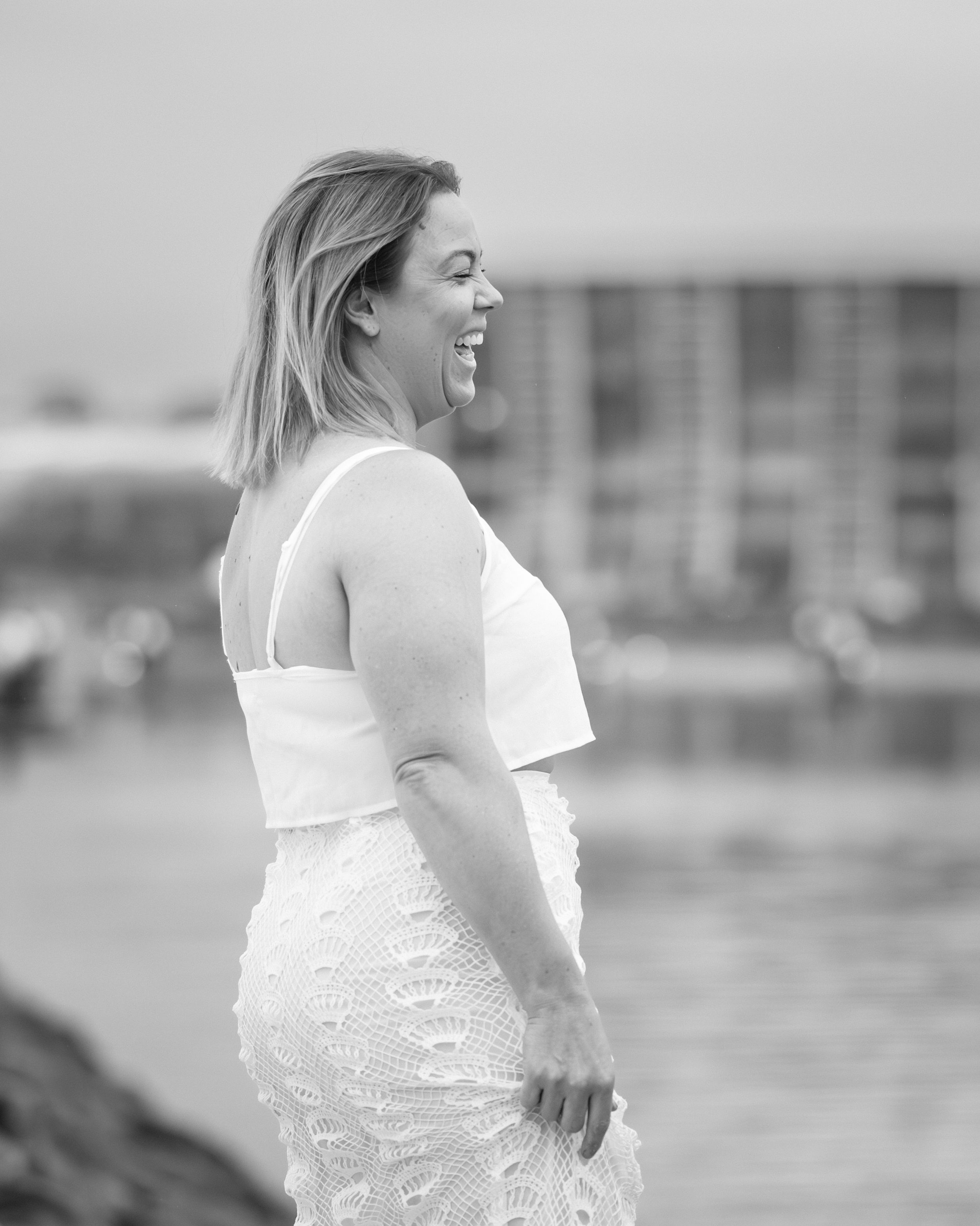 A person in a white lace dress poses on a beach during a photoshoot at sunset.