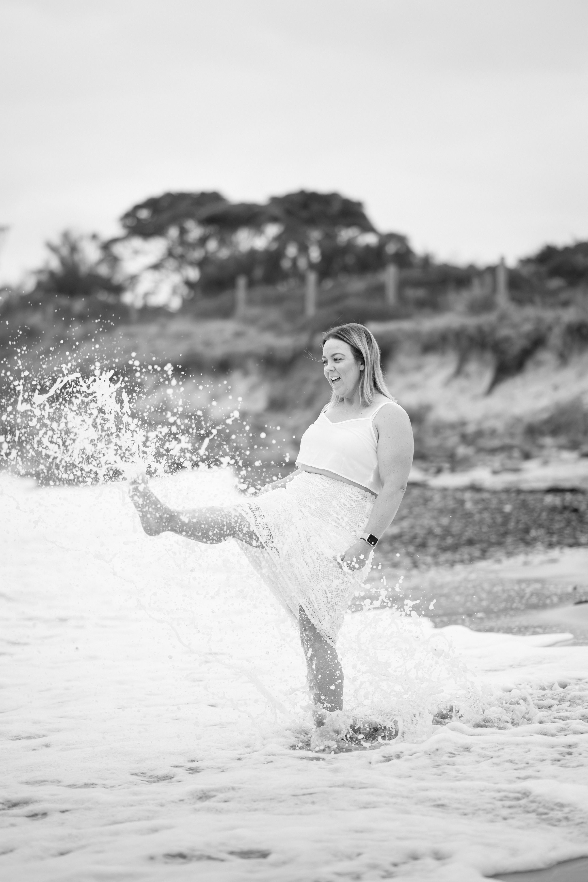 A person in white splashes through ocean waves along a scenic beach at sunset.