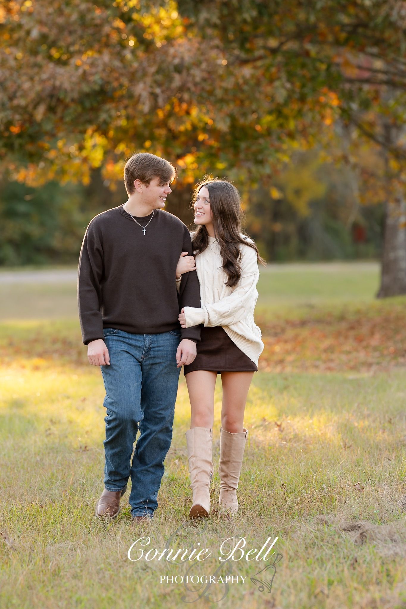 A couple in casual attire walks together through a golden autumn field during sunset.
