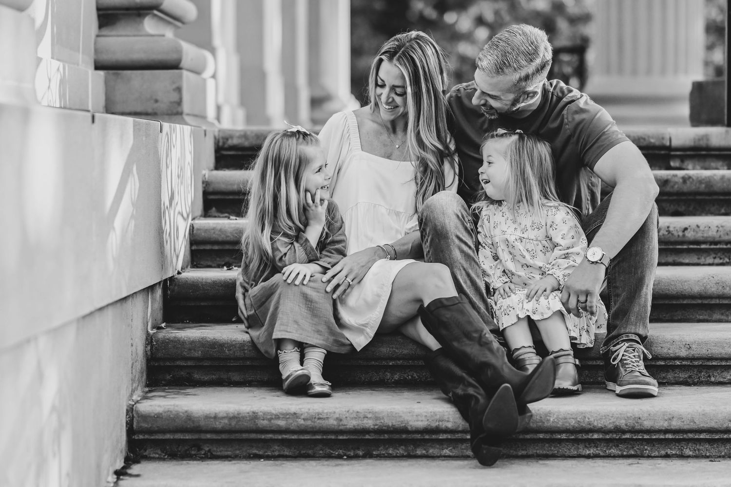Family sitting together on outdoor stone steps in casual black and white portrait.