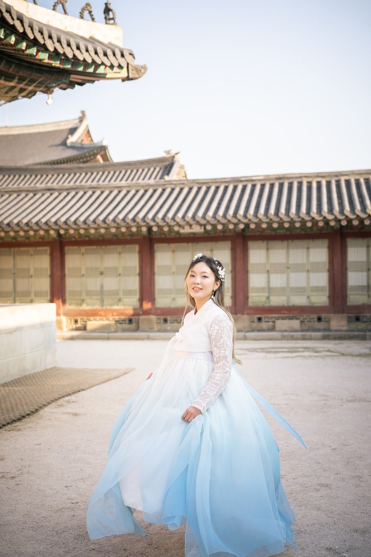 Traditional Korean hanbok dress in light blue and white flows gracefully against palace courtyard architecture.