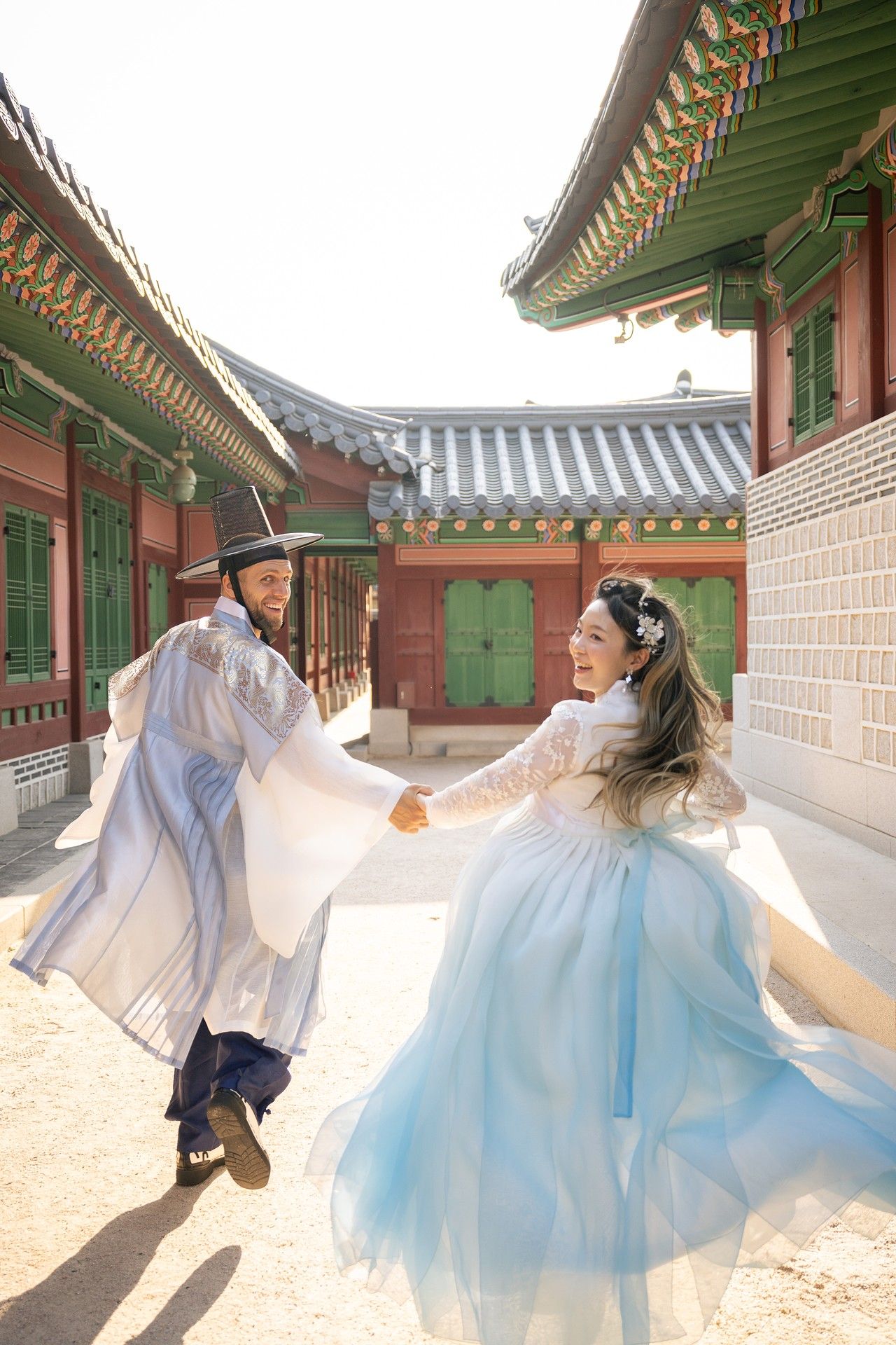 Couple in traditional Korean hanbok attire dancing and twirling together at a historic palace courtyard.
