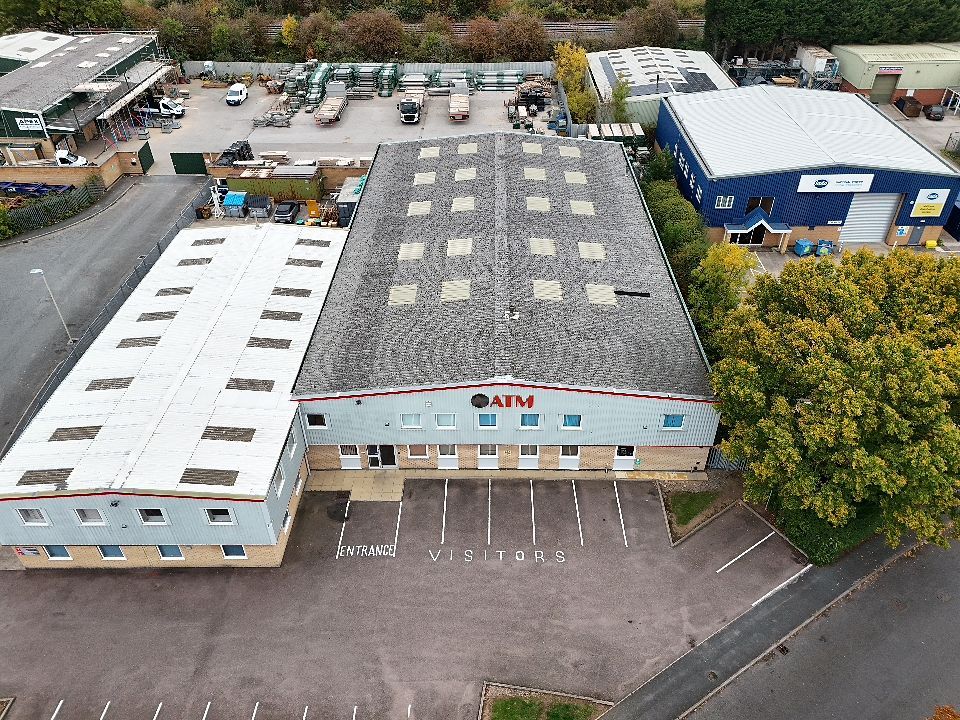 Aerial view of a commercial building with white roof and parking lot surrounded by autumn trees.
