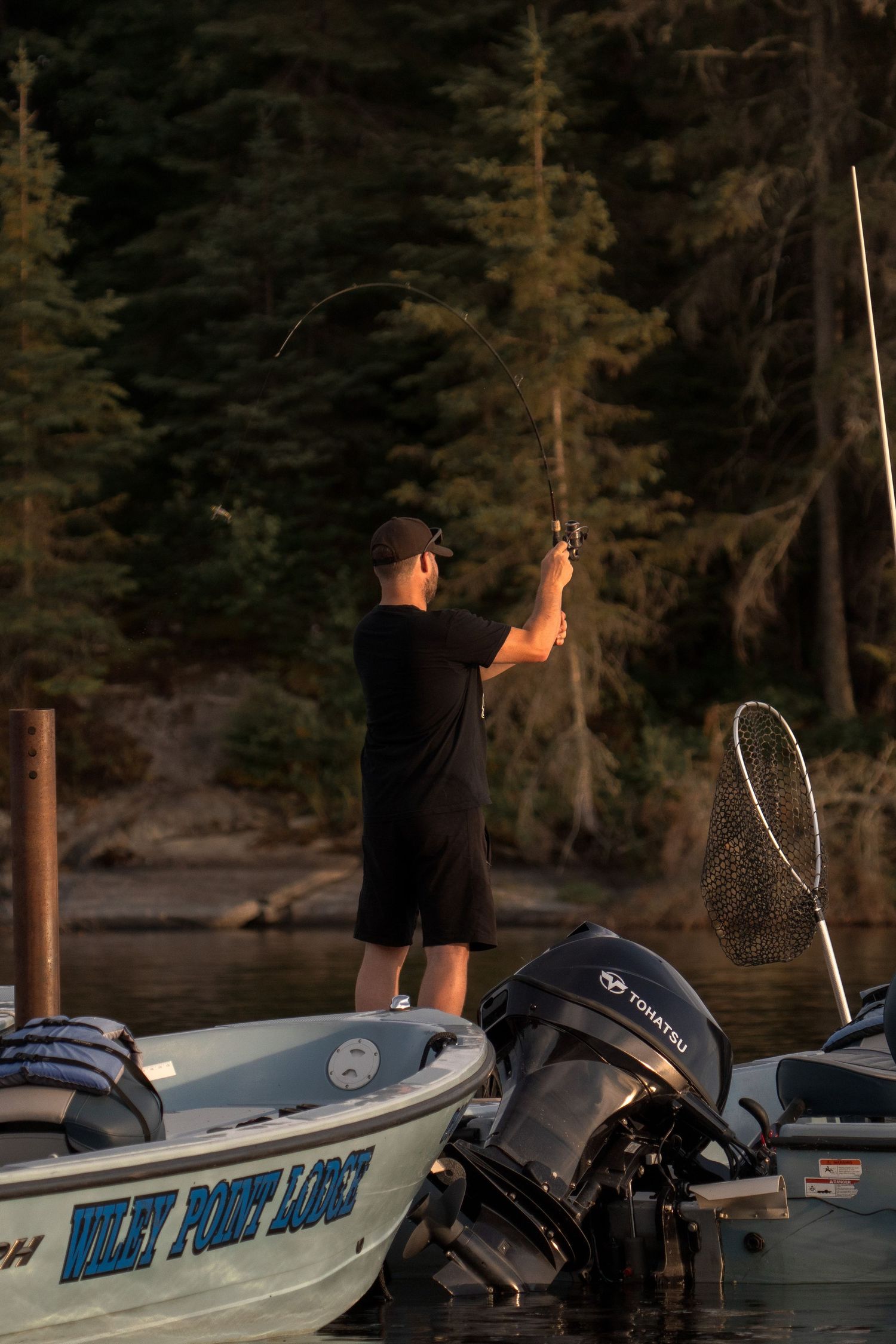 Silhouette of someone standing on a boat dock at sunset with fishing gear.