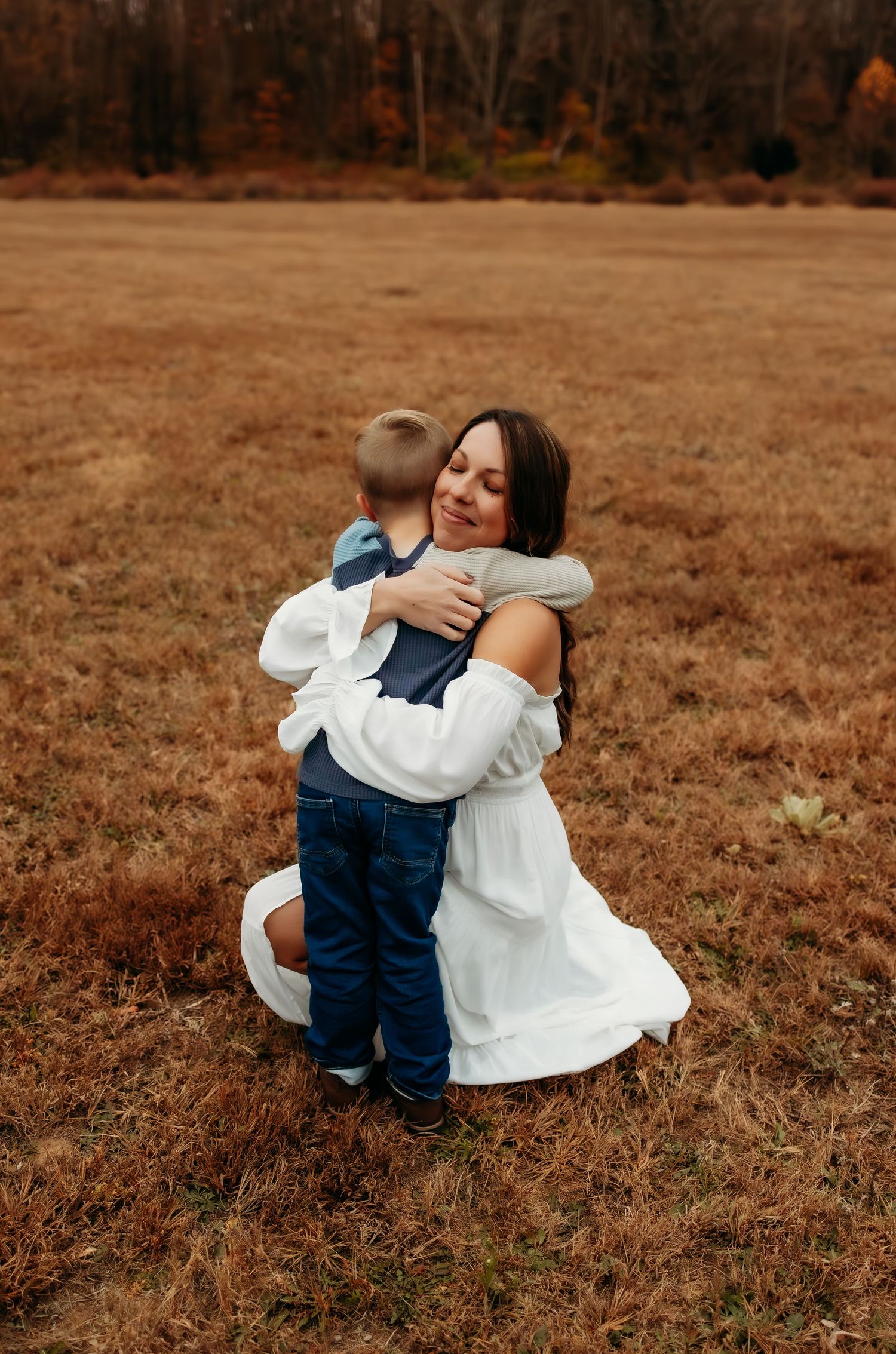 A touching moment captured in a fall field as a person in white embraces a small child wearing denim.
