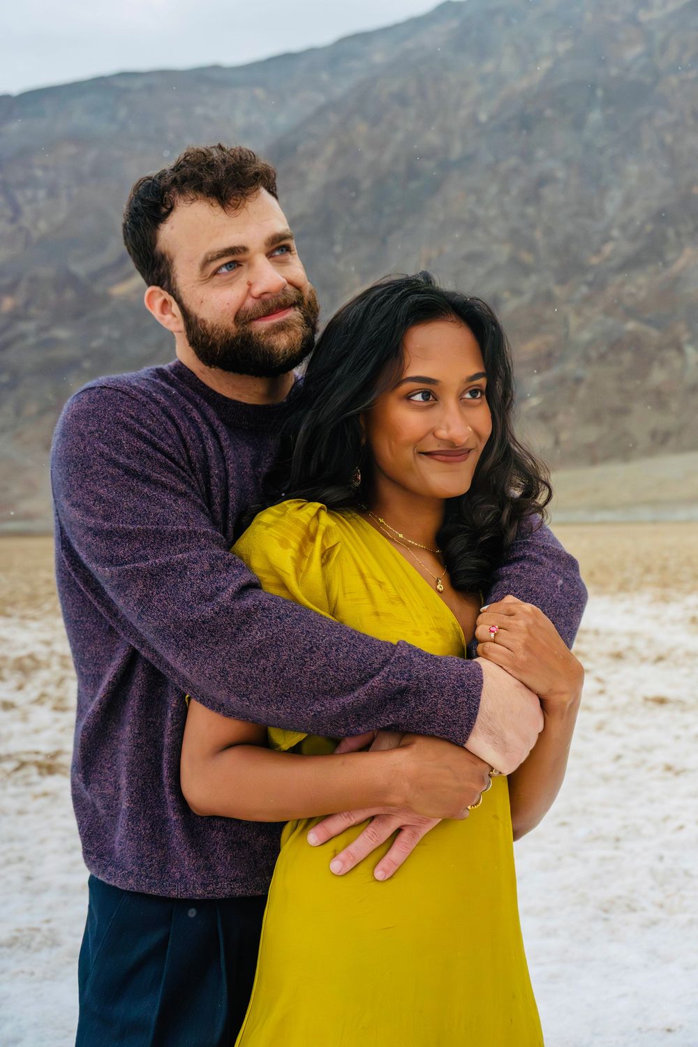 Couple sharing a tender embrace outdoors with arid mountain landscape in the background.