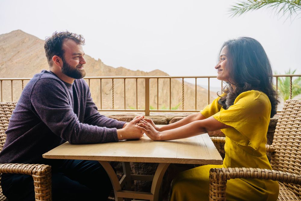 Couple sharing a tender moment holding hands at a table on a balcony overlooking desert mountains.
