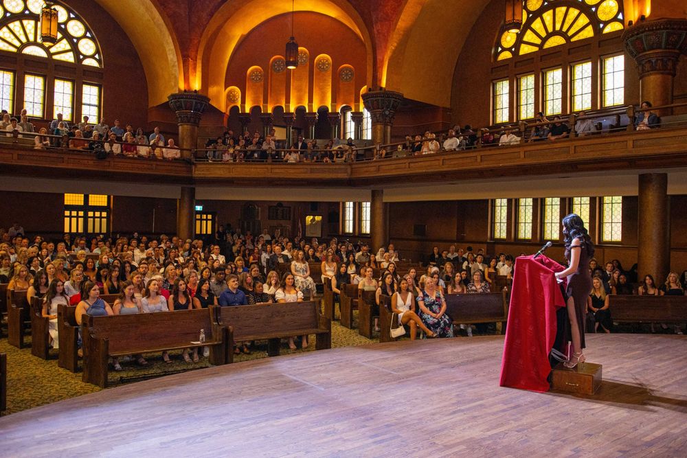 Large audience gathered in an ornate auditorium with arched ceilings and stained glass windows during a ceremony.