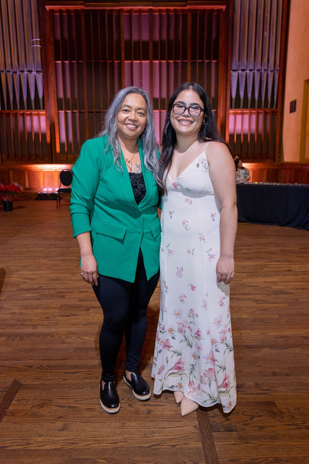 Two guests pose together at a formal event with organ pipes visible in the background.