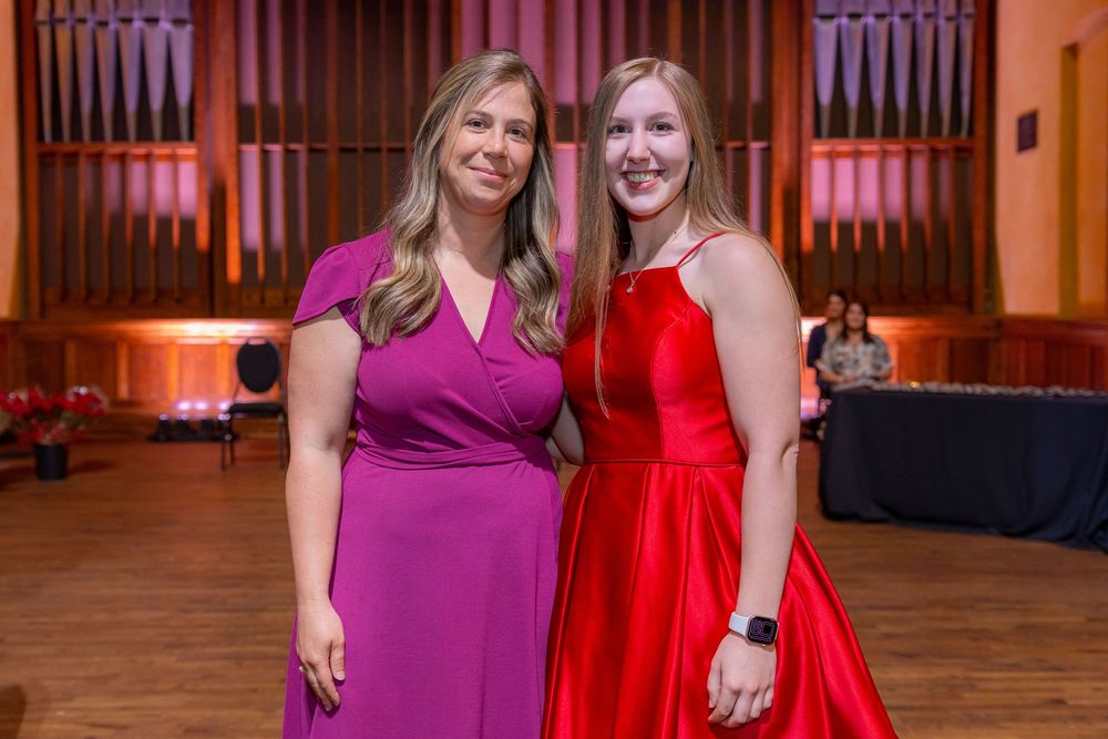 Two attendees in elegant evening dresses pose at a formal event with red lighting.
