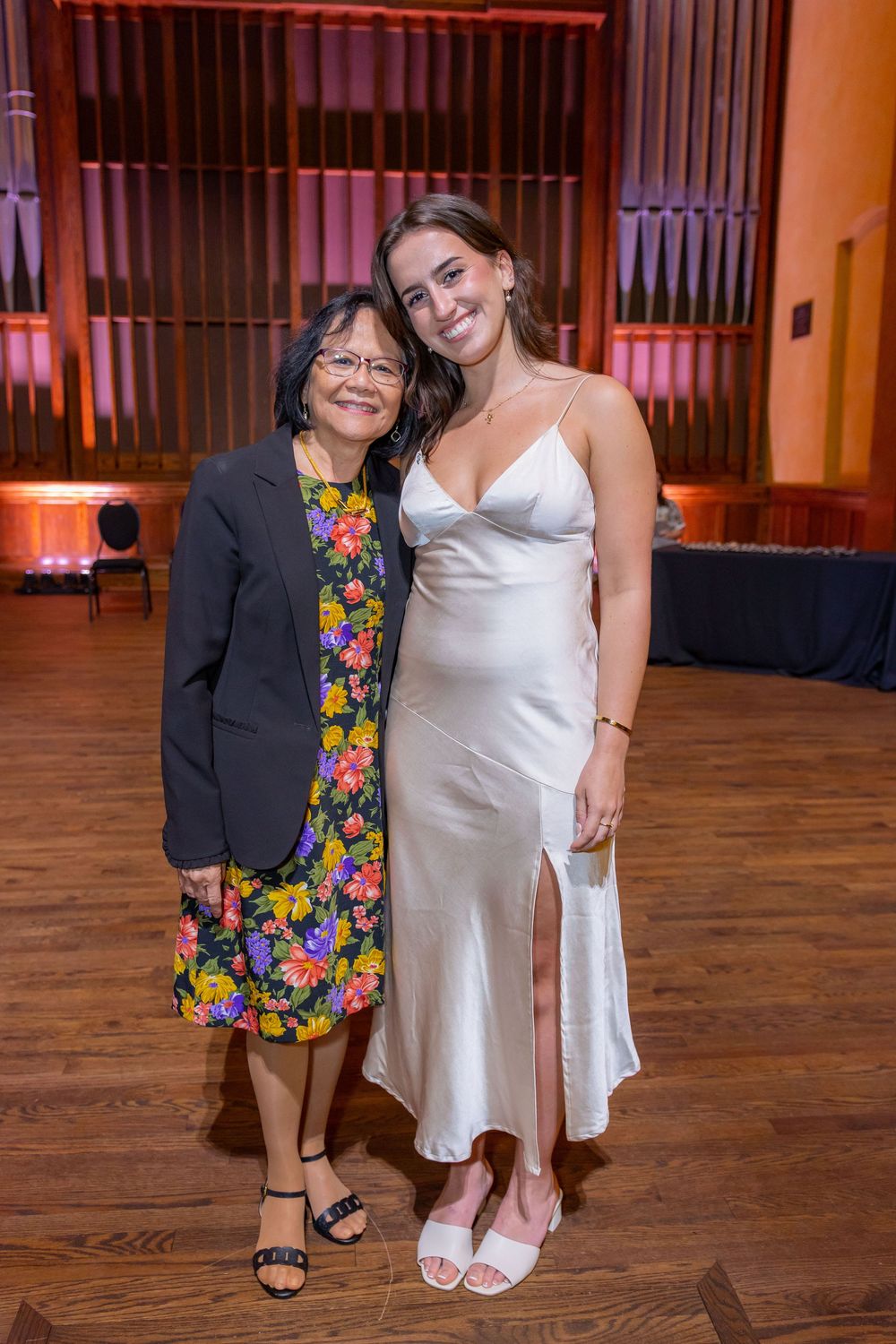 Two attendees stand together on wooden floors under warm lighting at a formal event.