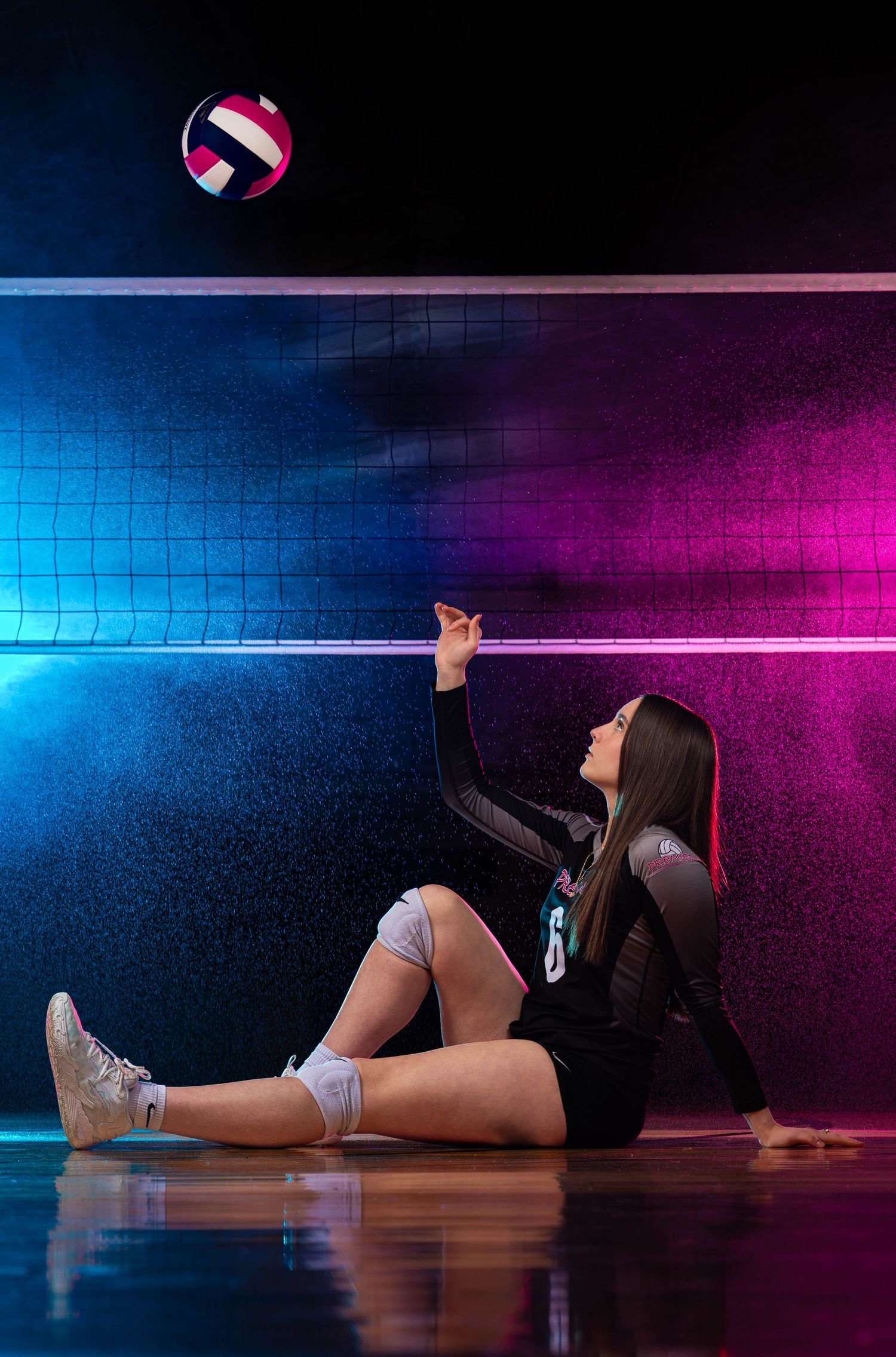 A volleyball player lies on the floor in a gym with dramatic blue and pink lighting.