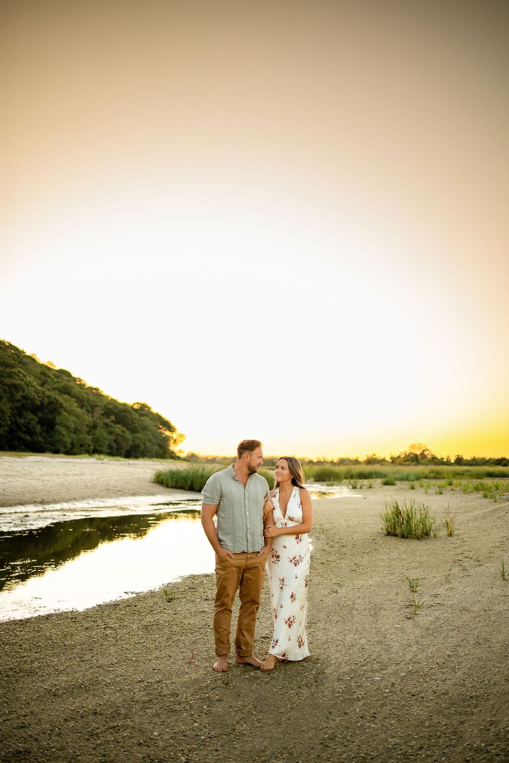 A couple walks together along a scenic beach shoreline during golden hour sunset.