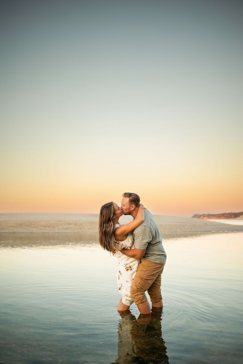 A romantic couple stands in shallow ocean water at sunset sharing an intimate moment against a serene coastal backdrop.