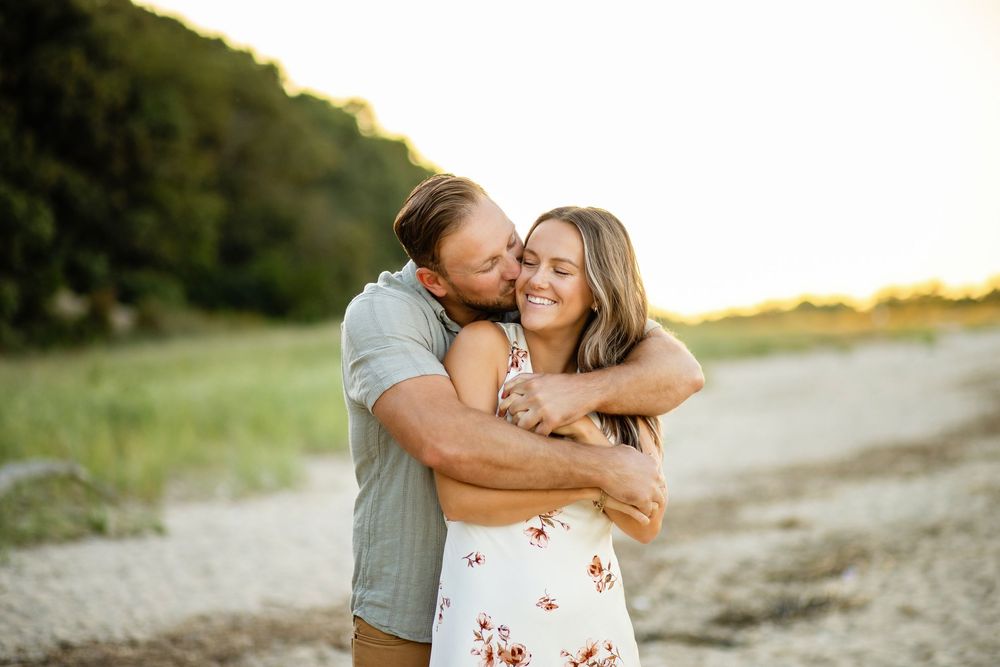 Romantic couple embraces and kisses during golden hour photoshoot in a natural outdoor setting.