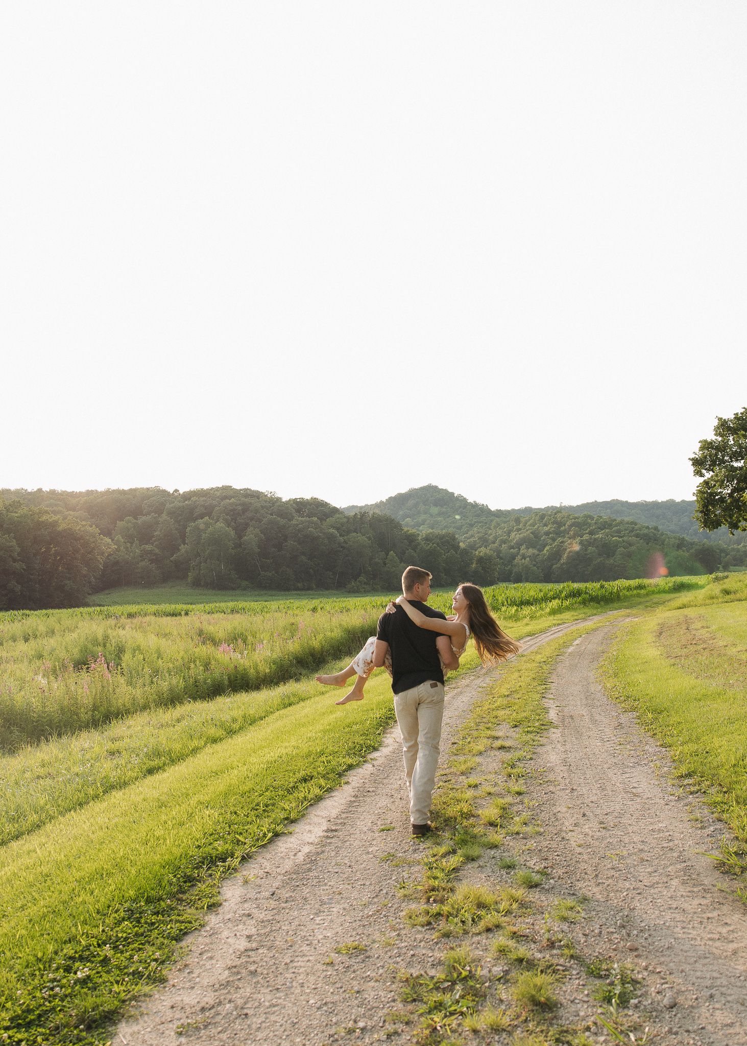 Couple walking hand in hand through a golden meadow path surrounded by tall grasses at sunset.