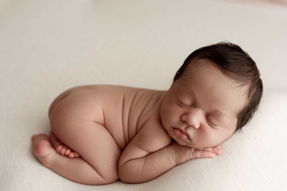 A sleeping newborn baby rests peacefully in a curled up position on a soft white blanket. – newborn photographer Paloma Schell Houston TX