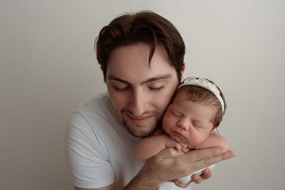 A tender moment between a parent and sleeping newborn baby in a minimalist portrait against a light background– newborn photographer Paloma