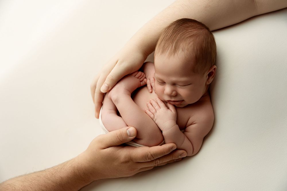 Newborn baby sleeping peacefully cradled in parents hands on white background.