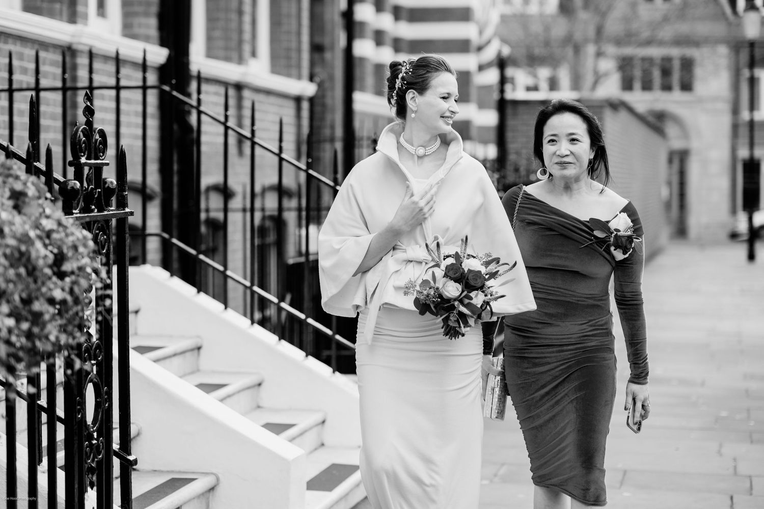 Two people in formal attire run joyfully down a city street while holding hands and smiling.