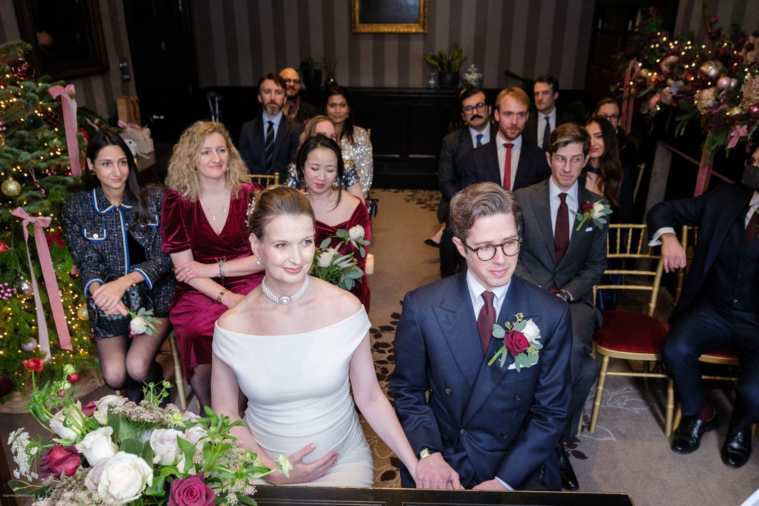 Wedding ceremony guests seated in rows with burgundy and floral decorations in an elegant indoor venue.