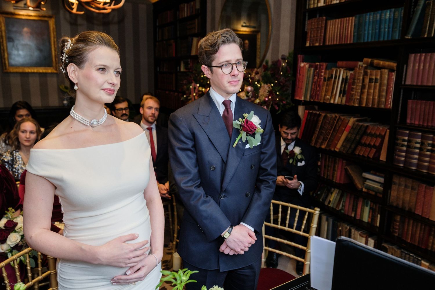 An elegant wedding ceremony in a library setting with bookshelves and chandelier lighting.