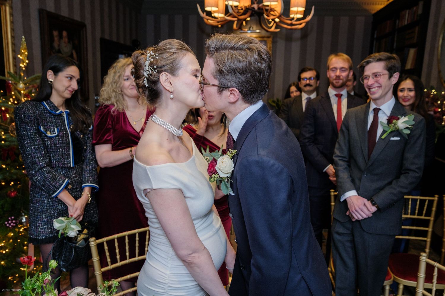A couple shares a romantic kiss at their elegant indoor wedding reception while guests look on.