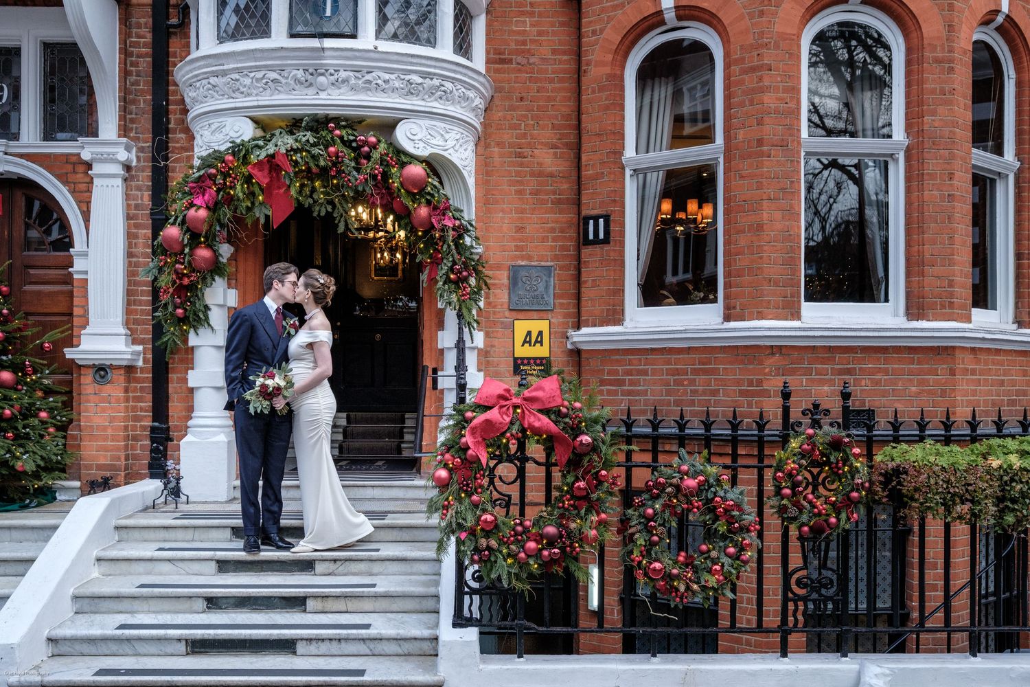 Red brick Victorian building entrance with white trim and decorative steps adorned with climbing roses.