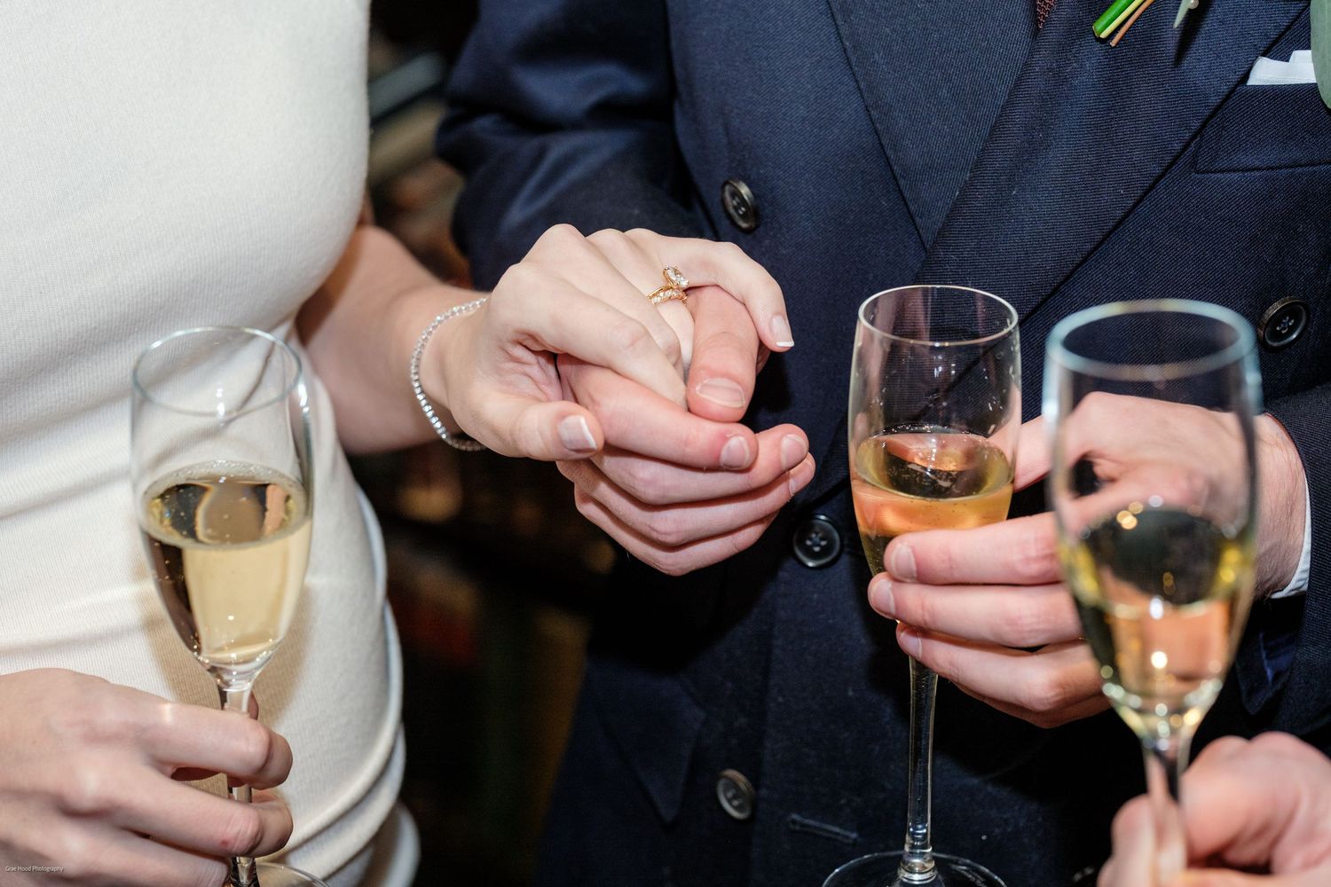 People holding wine glasses in a social gathering with hands visible against dark backgrounds.