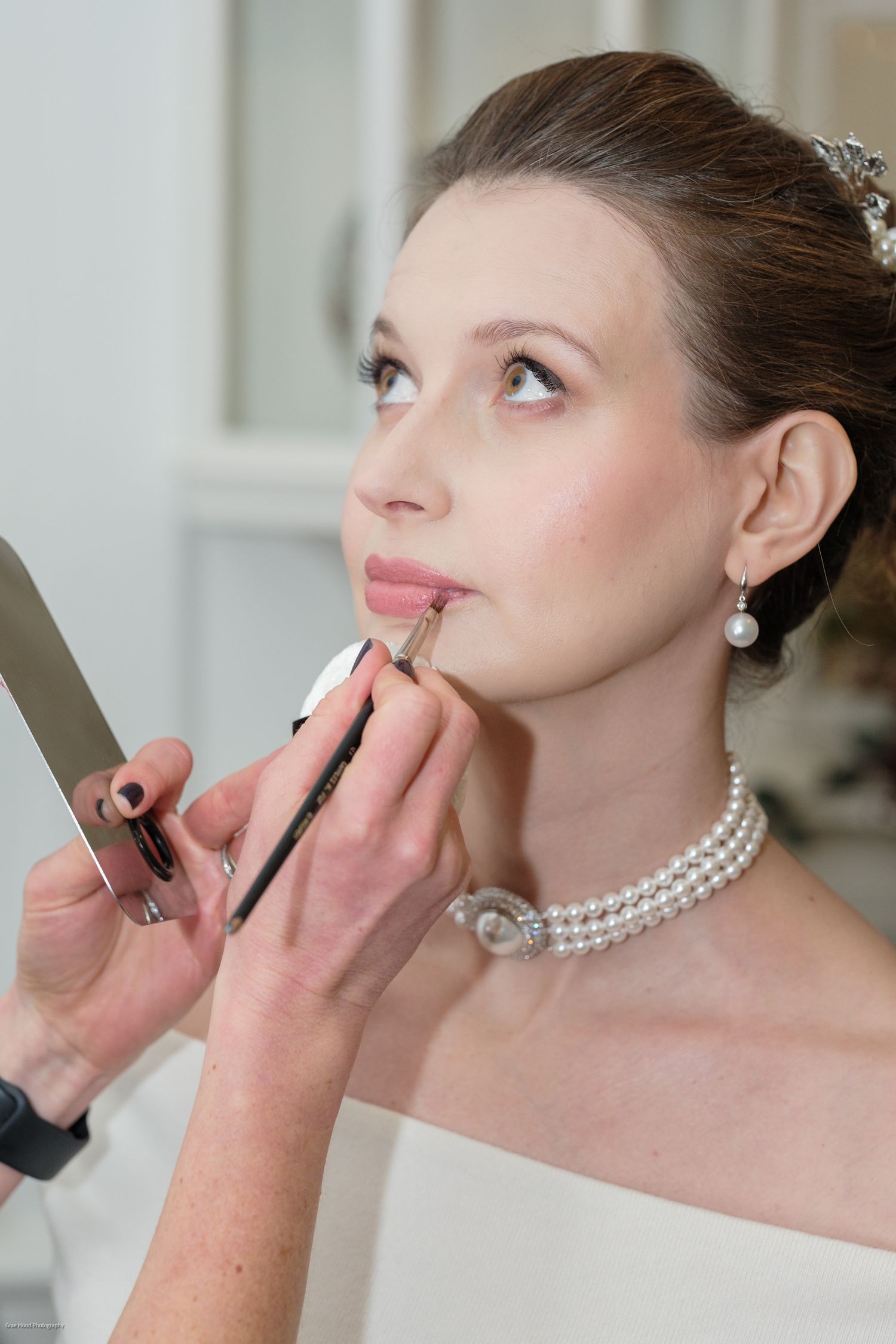 A makeup artist applies lipstick to a model wearing an elegant pearl necklace in a bridal preparation sequence.