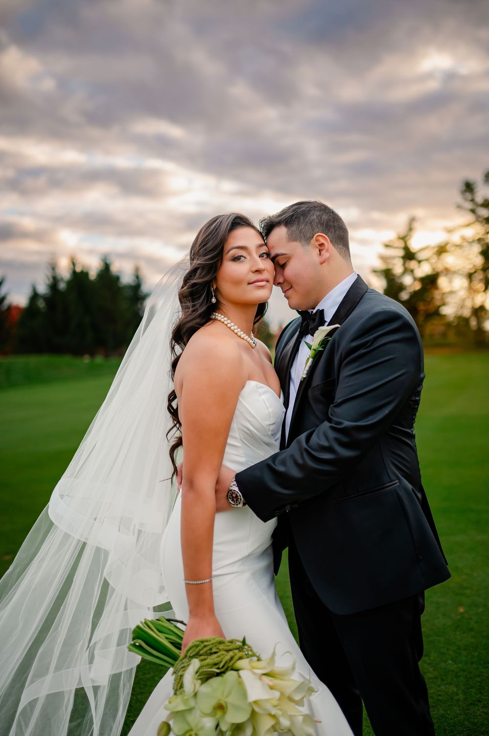 A romantic wedding couple shares intimate moments at sunset on a lush green golf course.