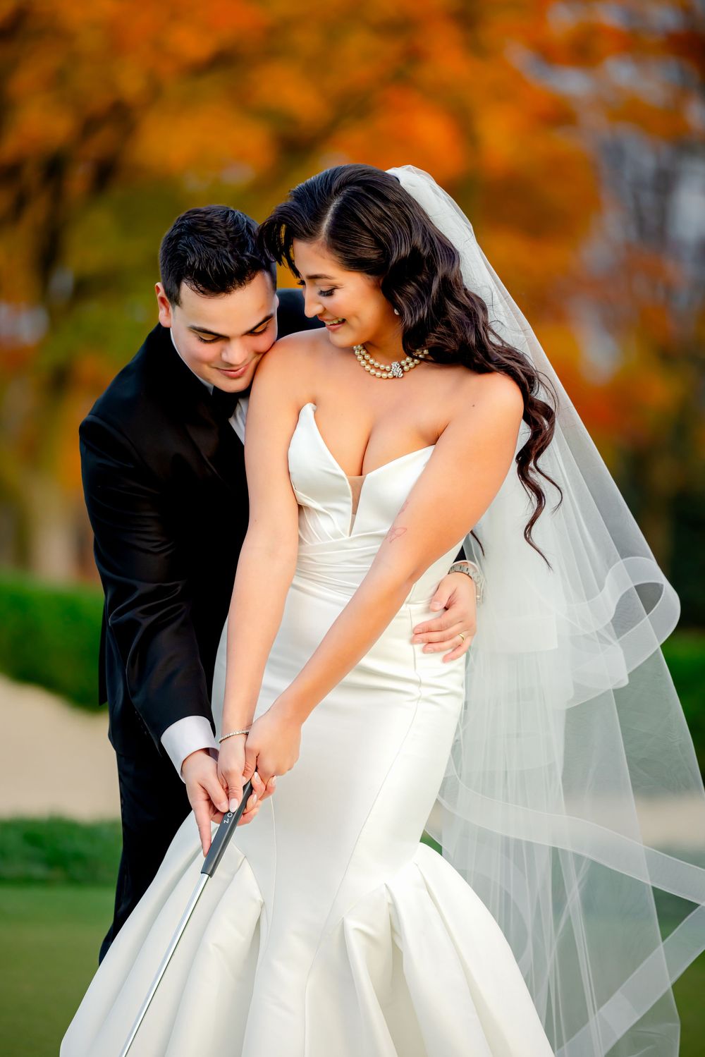 A romantic wedding couple embraces in an autumn setting with orange and golden fall foliage in the background.
