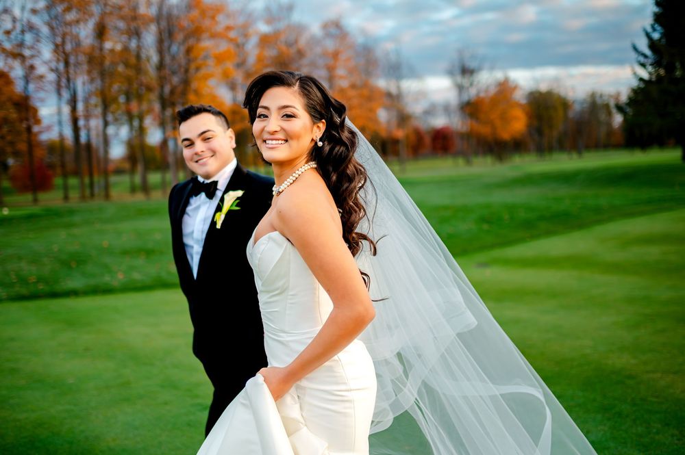 A couple shares a romantic moment on a lush golf course with autumn trees in the background.