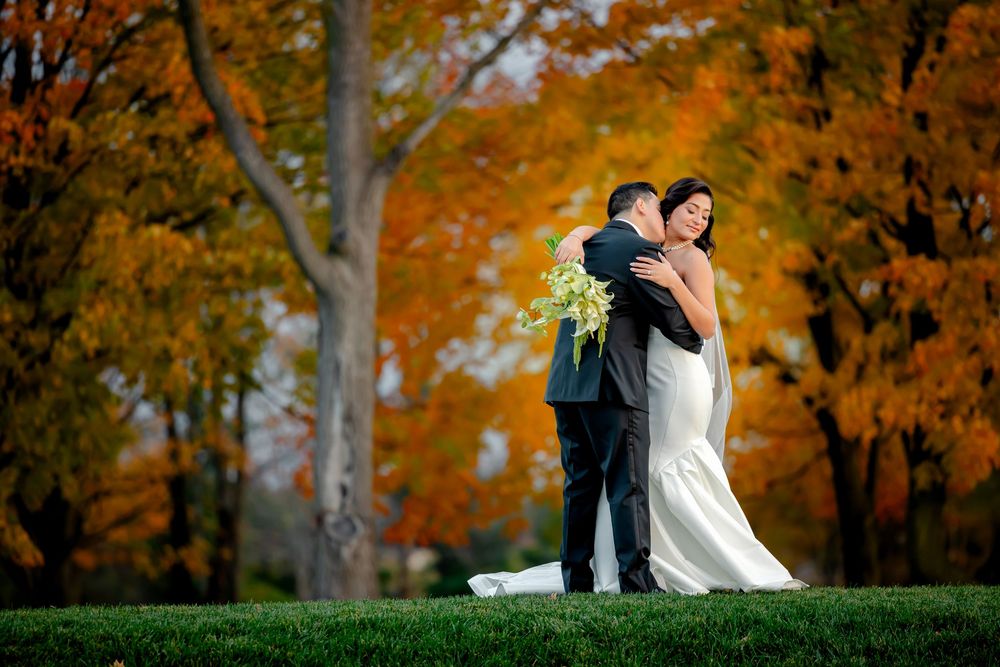 A couple embraces in an autumn setting with vibrant orange foliage and trees creating a romantic backdrop.