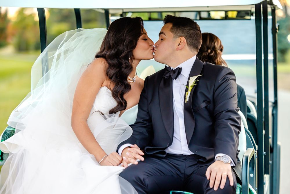 Romantic couple shares a tender kiss on their wedding day while sitting in a vintage car.