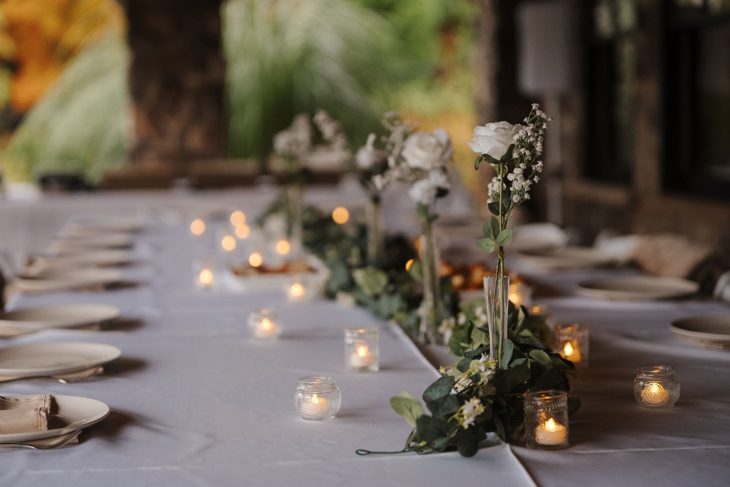 Elegant table setting with tealight candles and delicate floral arrangements along a white tablecloth.
