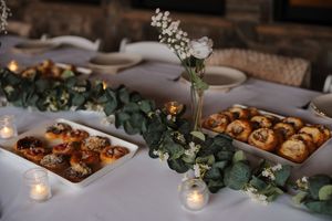 Elegant wedding reception table with pastries, eucalyptus garland, and glowing candles on white linens.