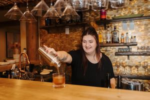 A series of people enjoying drinks at a rustic bar with exposed brick walls and wooden accents.