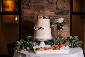 Elegant two-tier white wedding cake decorated with eucalyptus leaves and displayed on a rustic stone backdrop.
