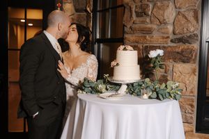 Newlyweds share an intimate moment while cutting their wedding cake at a rustic stone-walled venue.