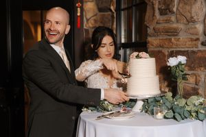 A couple cuts their elegant white wedding cake together at their reception in a rustic brick-walled venue.