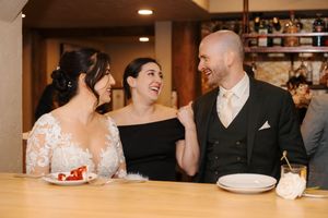 Three people share a joyful moment while seated at a bar counter during what appears to be a wedding celebration.