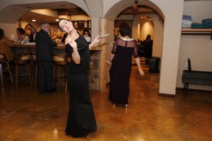 People dancing in pairs on a wooden dance floor at a social gathering in a warmly lit venue.