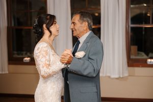 A couple in wedding attire dance and laugh together during their first dance at an indoor reception venue.