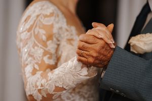 Close-up of hands holding each other during a wedding ceremony with delicate lace dress details visible.