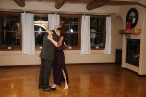 Dancers practicing together in a spacious dance studio with wooden beams and large windows at night.